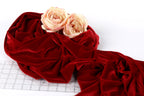 two white roses resting on a crumpled red velvet fabric.