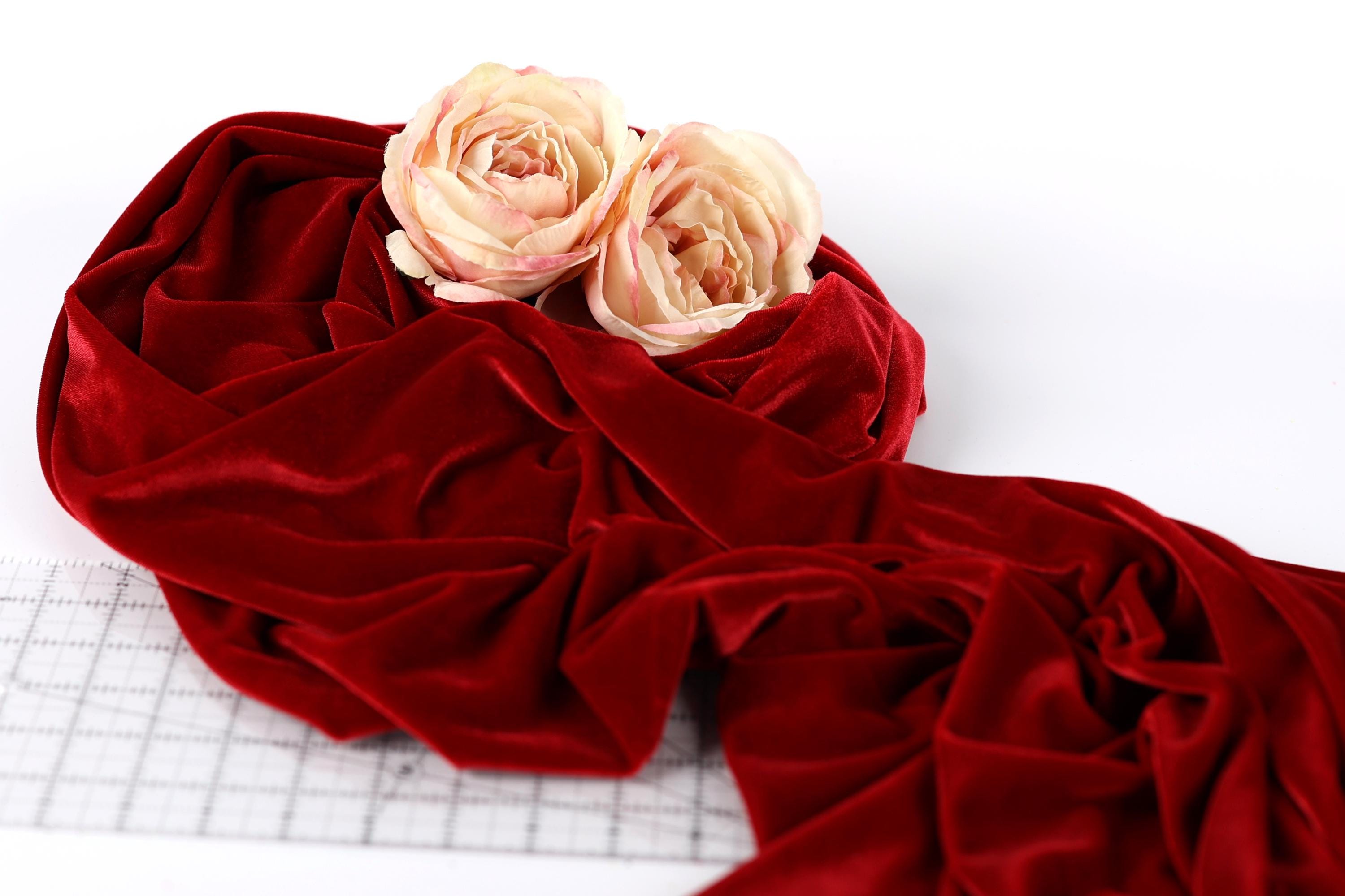 two white roses resting on a crumpled red velvet fabric.