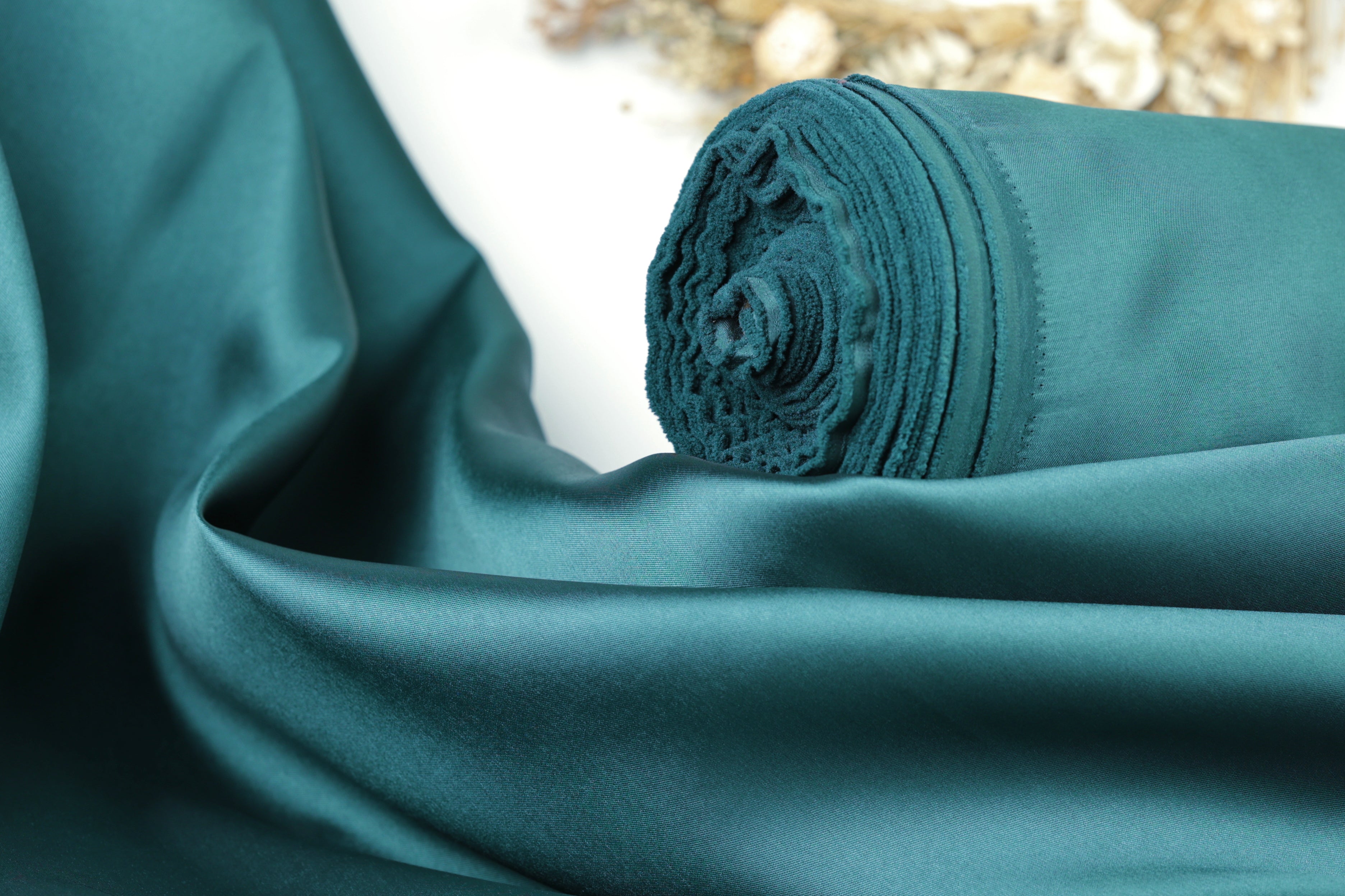 A close-up view of a rolled-up piece of dark green satin fabric.