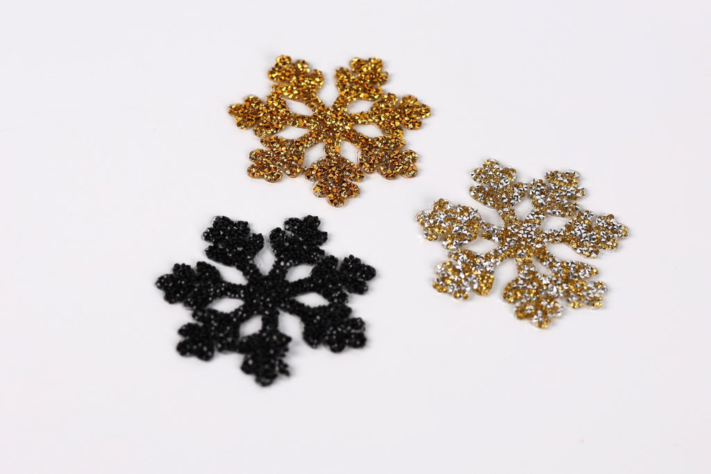 three glittery snowflake-shaped decorations, each with a unique color and design, arranged on a white background.