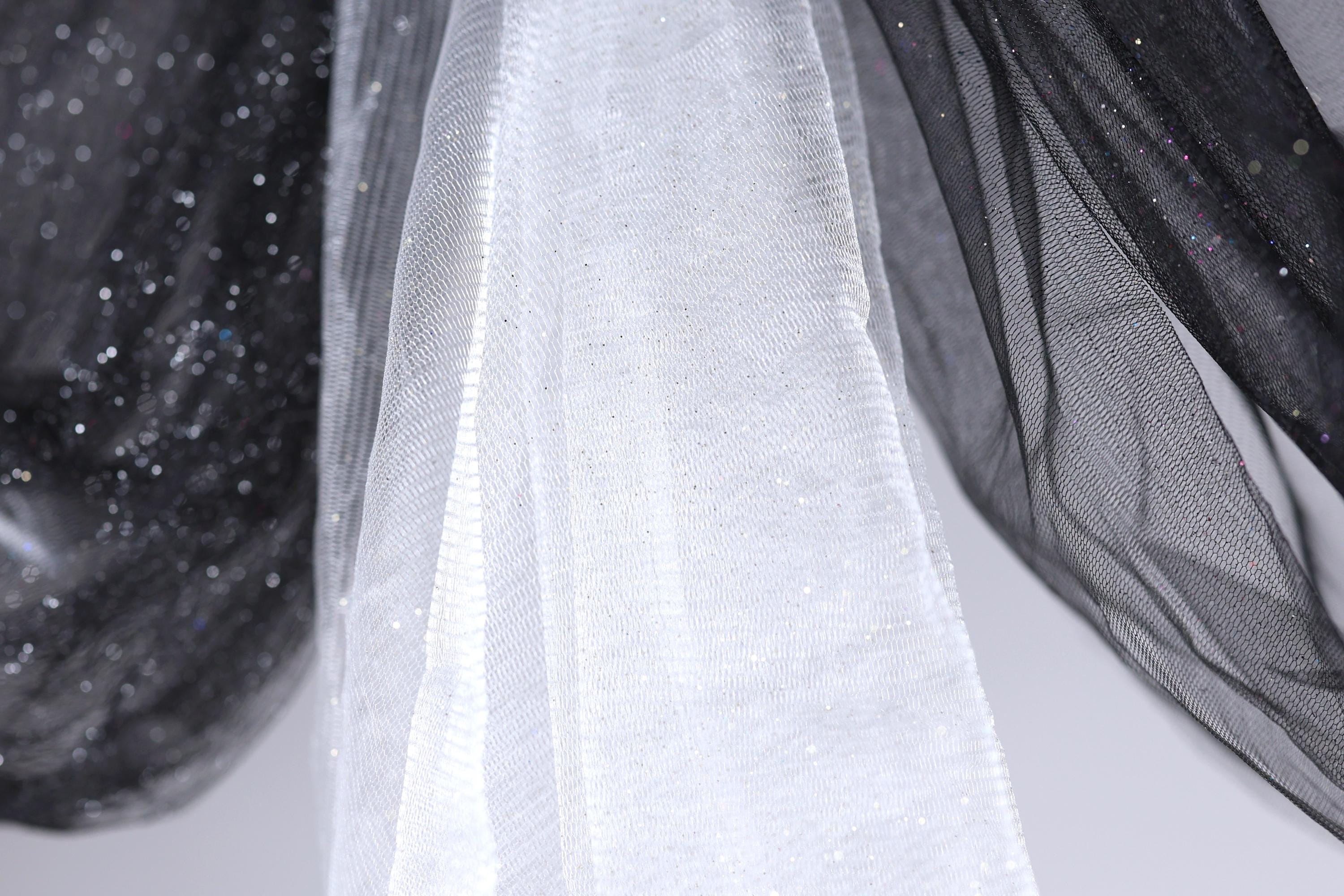 a close-up view of a white fabric with a black and white patterned design, hanging against a white background.