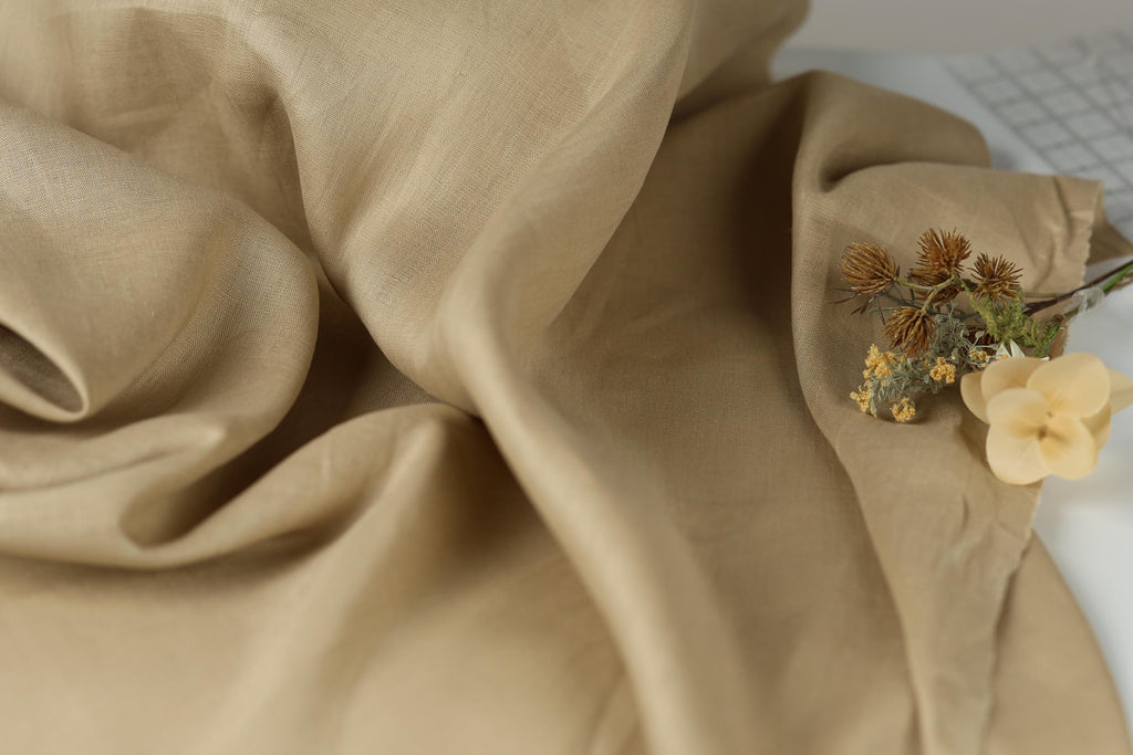 a close-up view of a crumpled beige fabric, with a small bouquet of dried flowers resting on top of it.