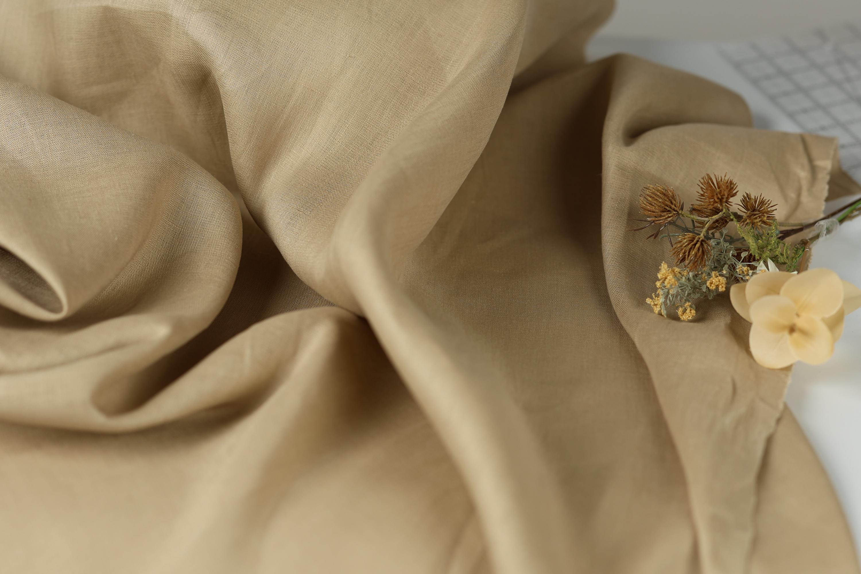 a close-up view of a crumpled beige fabric, with a small bouquet of dried flowers resting on top of it.