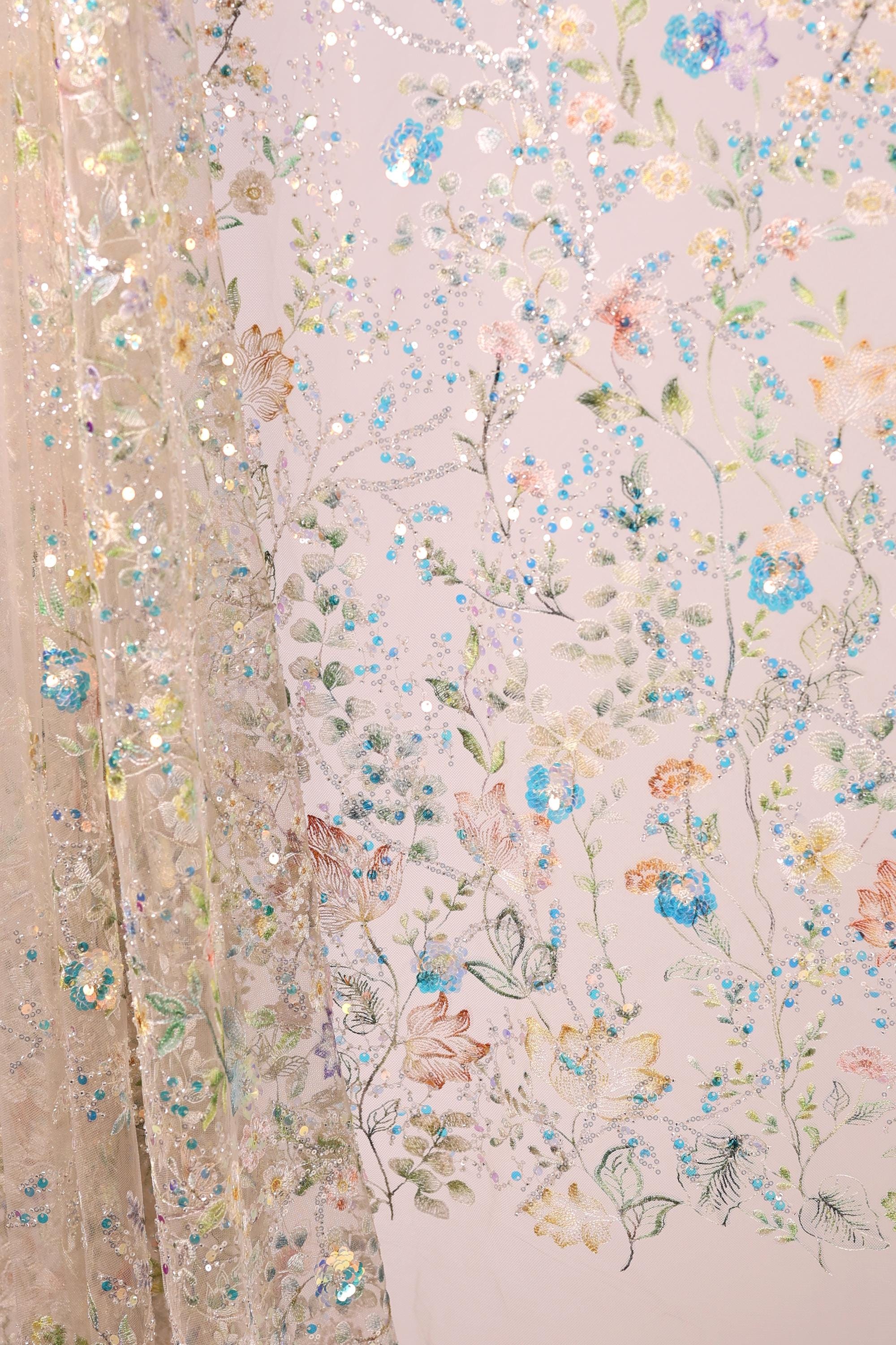 a close-up view of a delicate, intricately embroidered fabric with a floral pattern. The fabric is adorned with a variety of colorful flowers and leaves, creating a visually appealing and detailed design. The image showcases the craftsmanship and artistry involved in creating such a piece of textile art.
