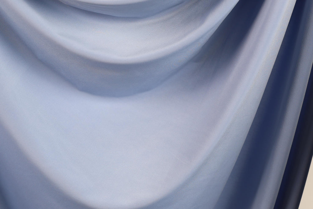 The image is a close-up of a blue fabric, possibly a piece of clothing or a textile. The fabric appears to be soft and smooth, with a subtle texture that suggests it might be made of silk or a similar material. The image does not contain any discernible objects or actions, and there are no specific details provided about the color or pattern of the fabric.