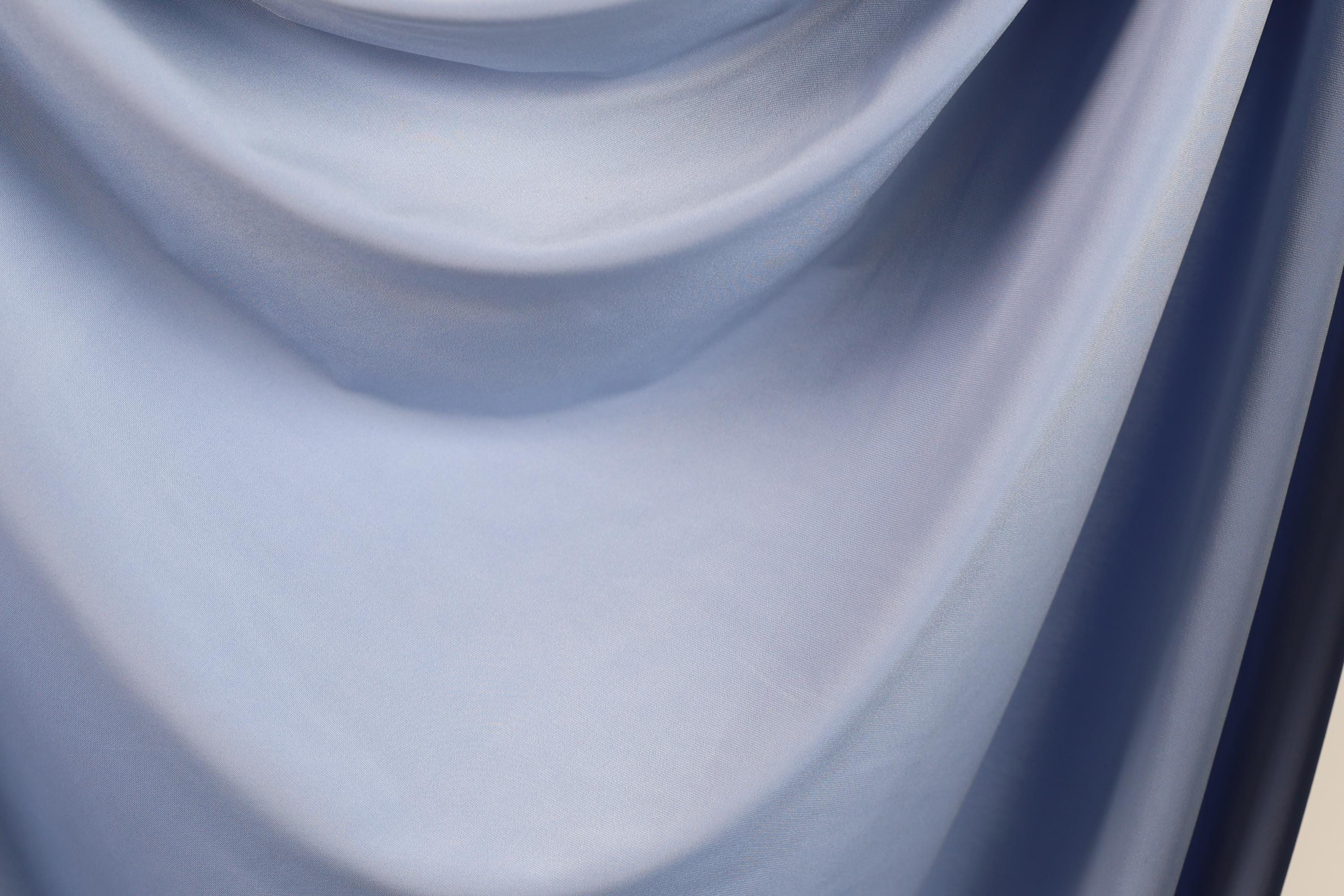 The image is a close-up of a blue fabric, possibly a piece of clothing or a textile. The fabric appears to be soft and smooth, with a subtle texture that suggests it might be made of silk or a similar material. The image does not contain any discernible objects or actions, and there are no specific details provided about the color or pattern of the fabric.