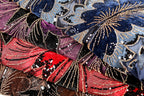 The image is a close-up of a fabric with a vibrant, colorful floral pattern. The fabric is adorned with numerous small beads and sequins, creating a visually striking and intricate design.