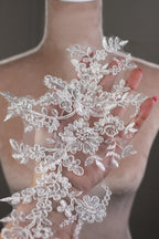 A hand holding a delicate, intricate piece of white lace with floral patterns.