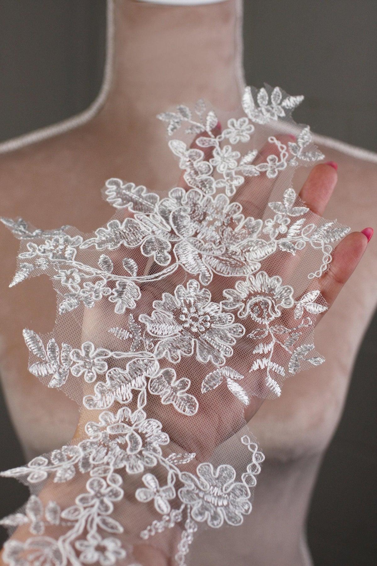 A hand holding a delicate, intricate piece of white lace with floral patterns.