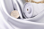 a close-up view of a piece of white fabric, possibly silk or satin, with a small circular object, possibly a badge or label, placed on it.