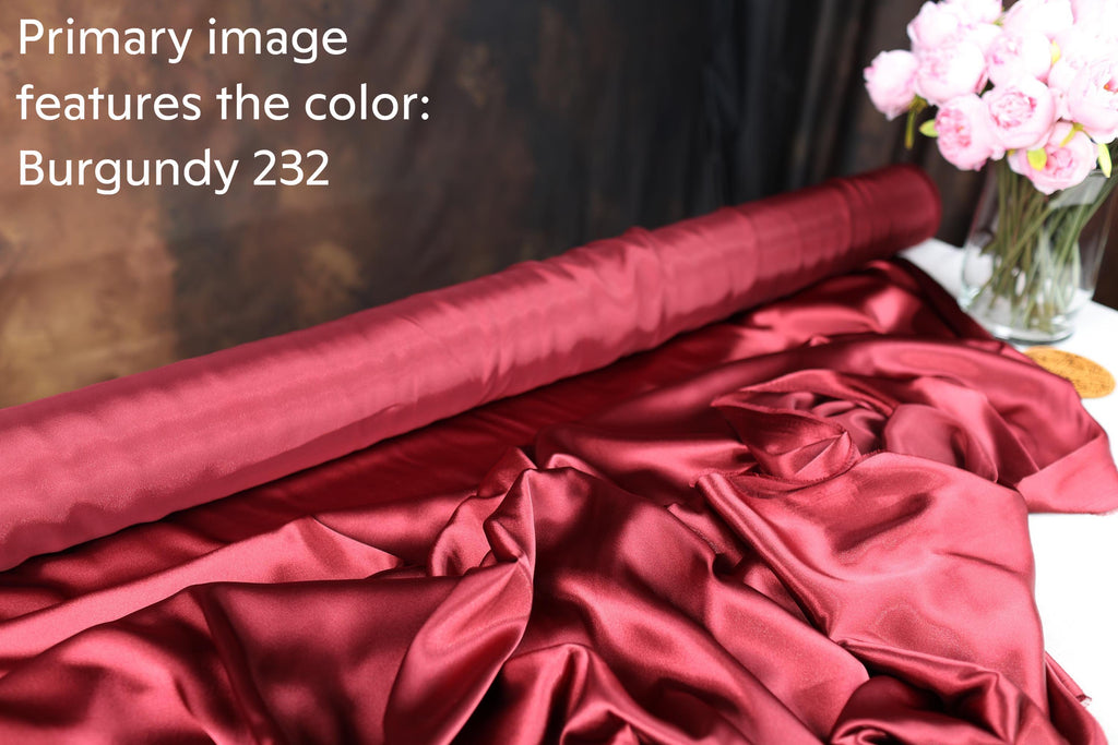a roll of burgundy fabric with a vase of pink flowers on a table.