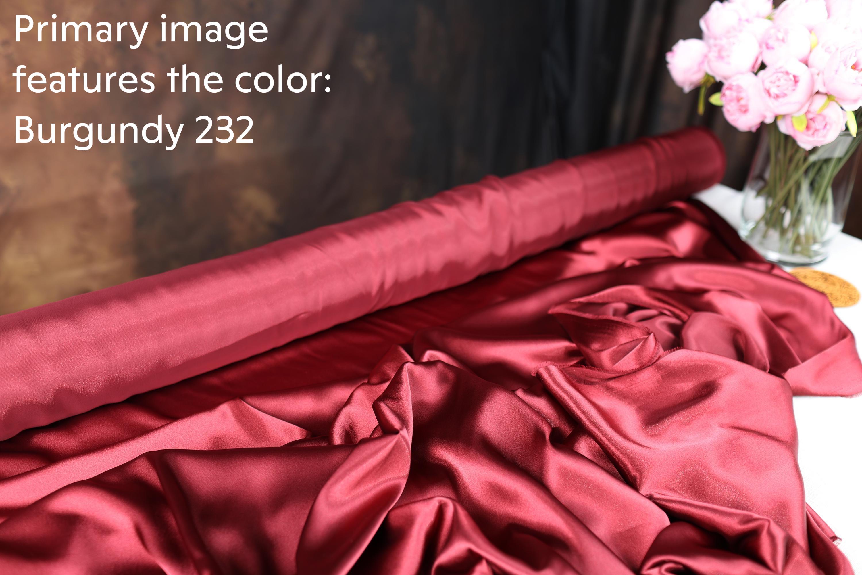 a roll of burgundy fabric with a vase of pink flowers on a table.