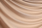 The image is a close-up of a light brown fabric, possibly silk or chiffon, with a smooth, flowing texture.