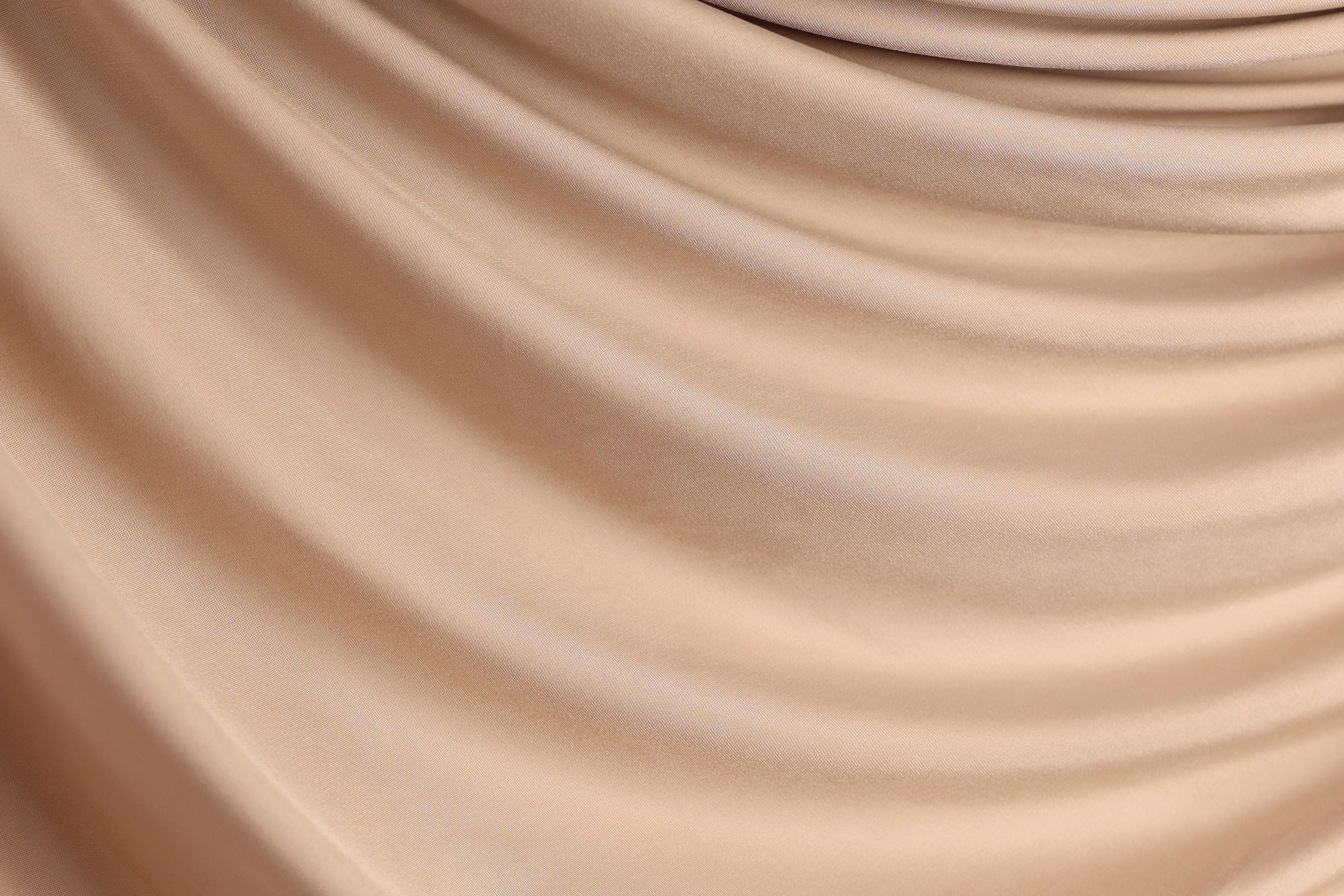 The image is a close-up of a light brown fabric, possibly silk or chiffon, with a smooth, flowing texture.