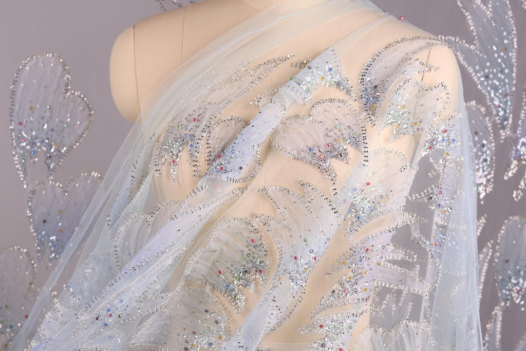 a mannequin wearing a white dress with intricate silver and blue embellishments, including sequins and beads, creating a sparkling and elegant appearance.