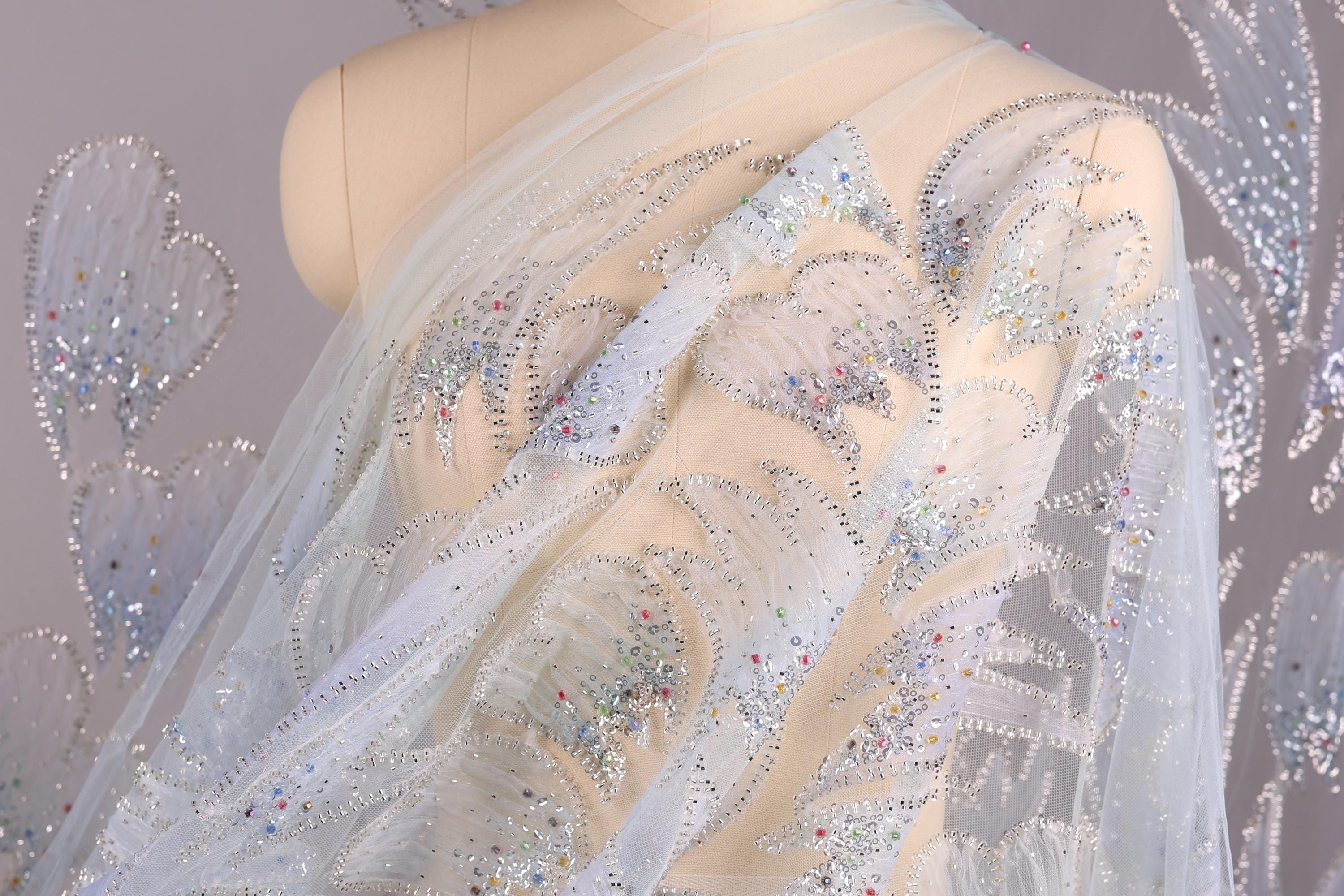 a mannequin wearing a white dress with intricate silver and blue embellishments, including sequins and beads, creating a sparkling and elegant appearance.