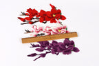 a collection of colorful flower embroidery pieces, including red, pink, and purple flowers, arranged on a wooden ruler for size comparison.