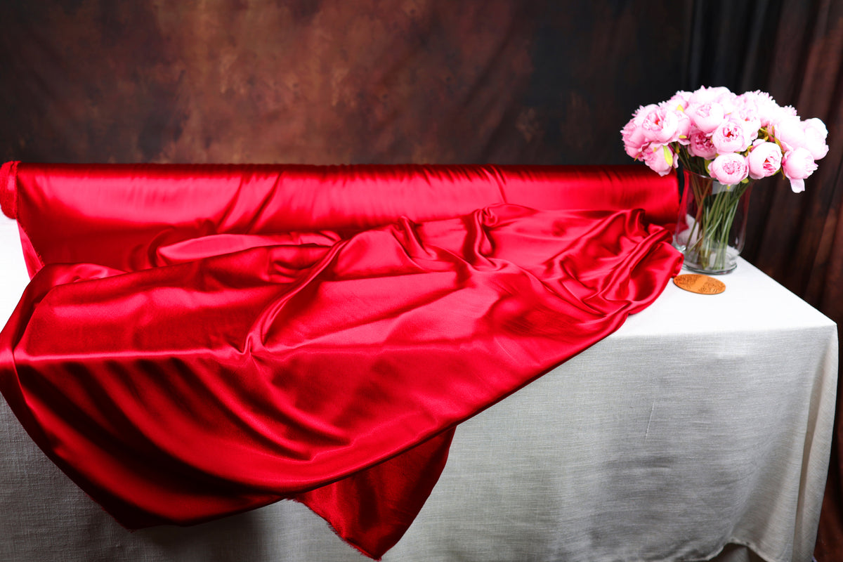 a red satin fabric draped over a white tablecloth, with a vase of pink flowers placed on the table.
