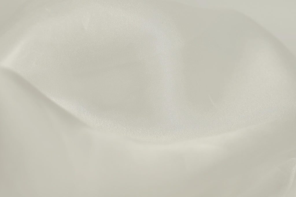 The image is a close-up of a white fabric, possibly silk or satin, with a smooth and shiny texture.