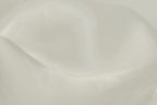 The image is a close-up of a white fabric, possibly silk or satin, with a smooth and shiny texture.