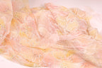 a close-up view of a delicate, sheer fabric with a floral pattern in shades of pink and yellow. The fabric appears to be made of sheer material, giving it a soft and delicate appearance.