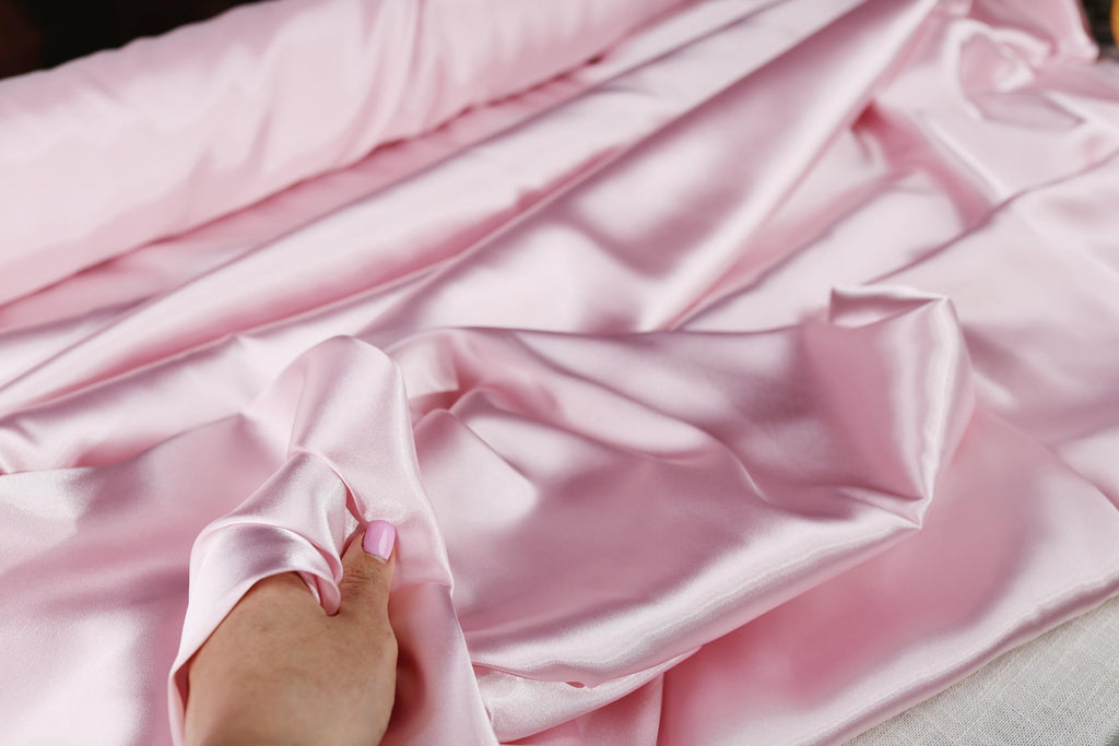 a person's hand on a pink satin material
