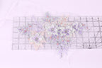 a collection of delicate, pastel-colored flowers and leaves, with some embellished with small beads, arranged on a transparent surface.