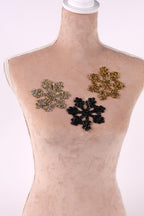 A mannequin is wearing a beige dress with three decorative snowflake-shaped embellishments in different colors - gold, black, and silver.