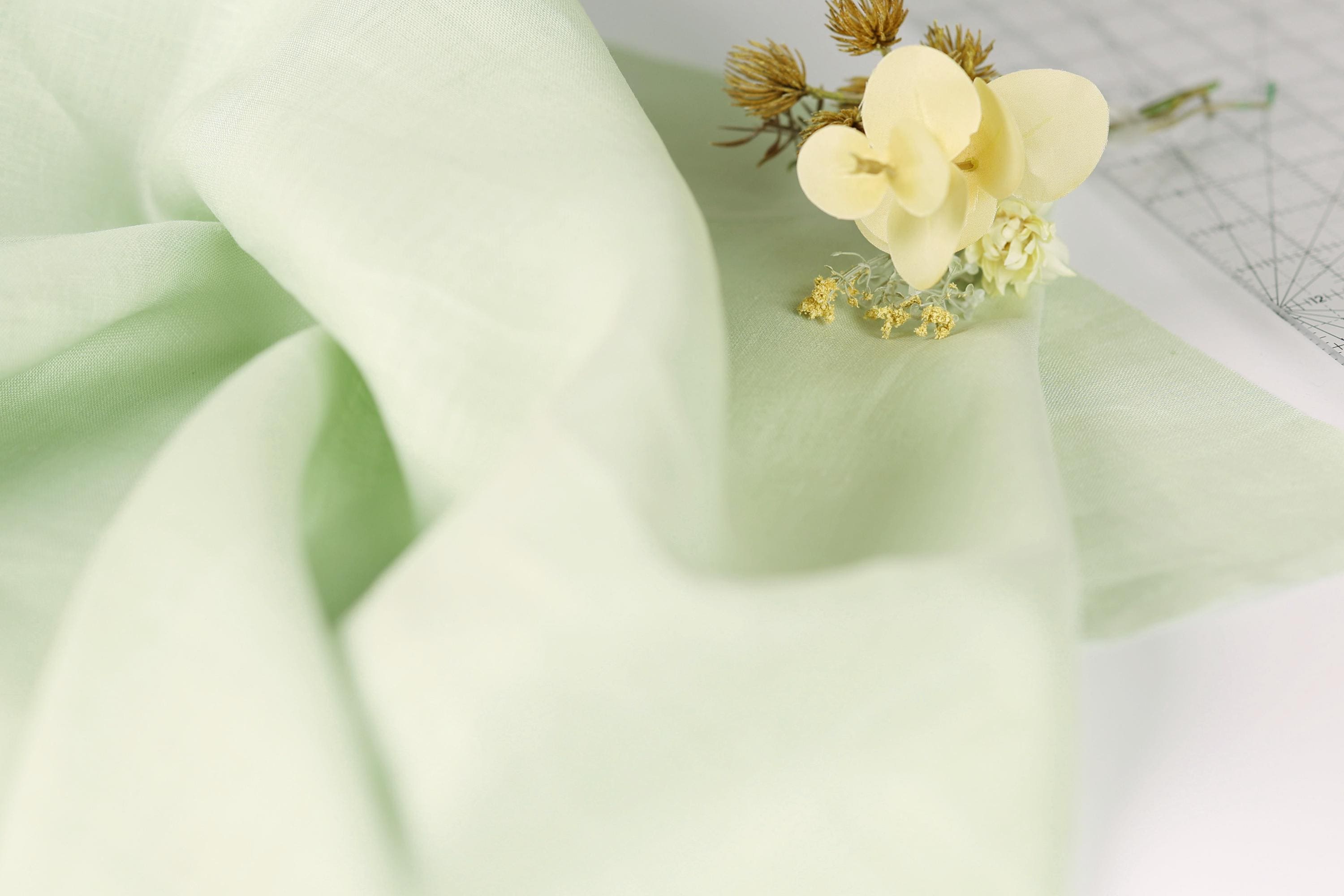 a close-up view of a delicate flower resting on a soft, light green fabric.