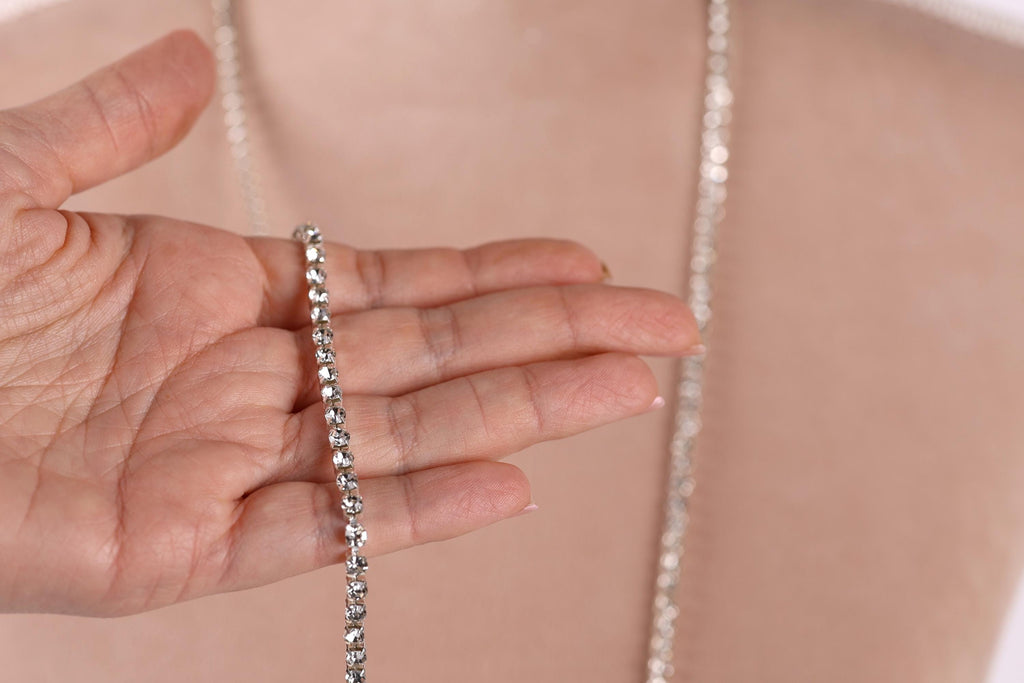 A close-up of a hand holding a silver necklace against a blurred background.