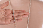 A close-up of a hand holding a silver necklace against a blurred background.