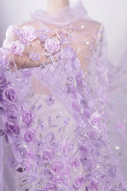 A close-up view of a delicate, hand-embroidered fabric with a floral pattern in shades of purple and white.