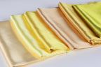 A row of folded fabric pieces in various shades of yellow, ranging from pale to deep, arranged on a white surface.