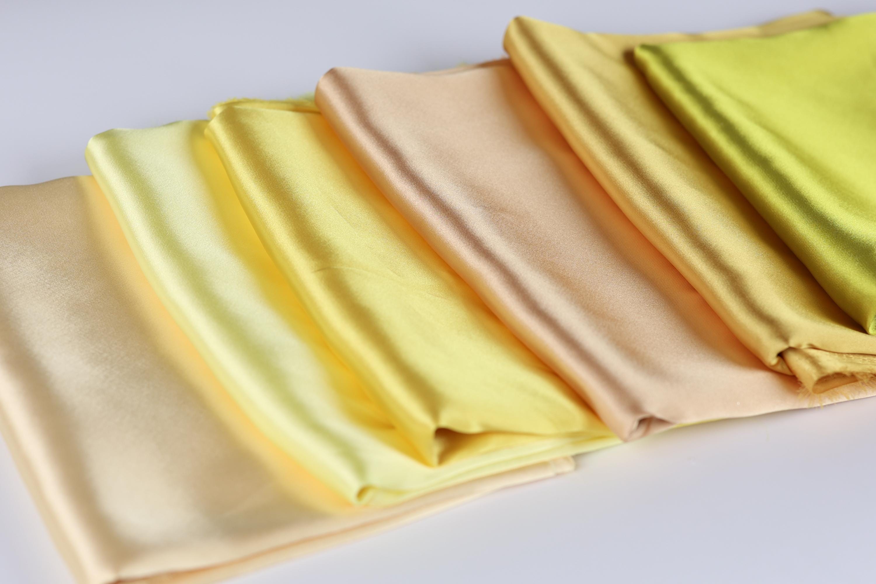 A row of folded fabric pieces in various shades of yellow, ranging from pale to deep, arranged on a white surface.