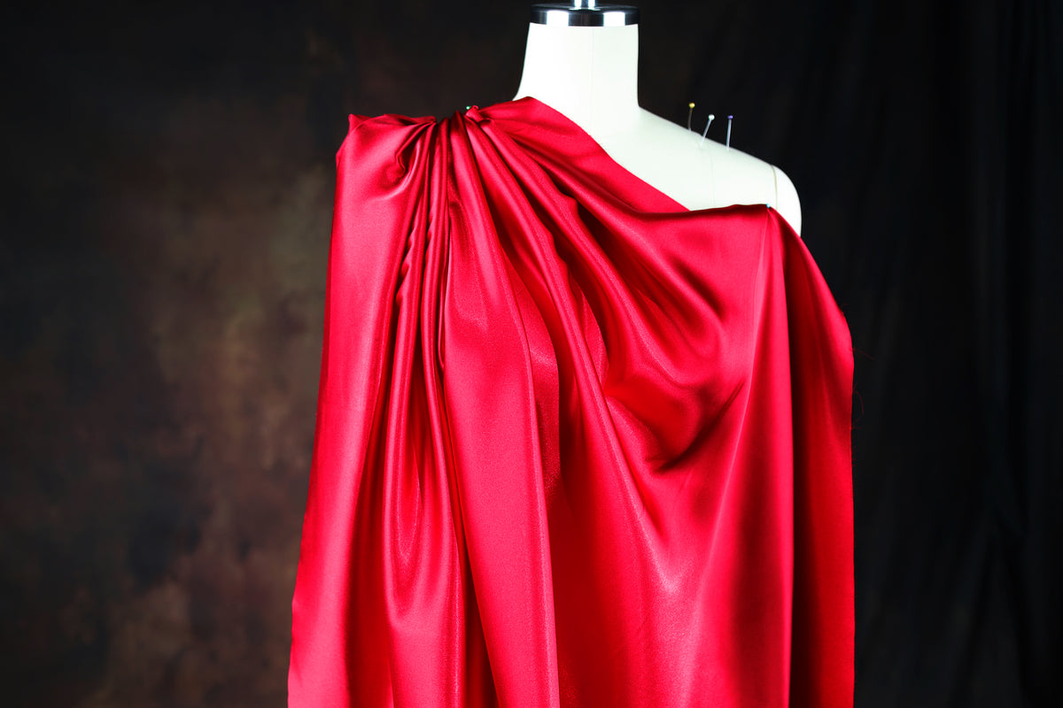 A mannequin wearing a red satin cape with a draped, flowing design.