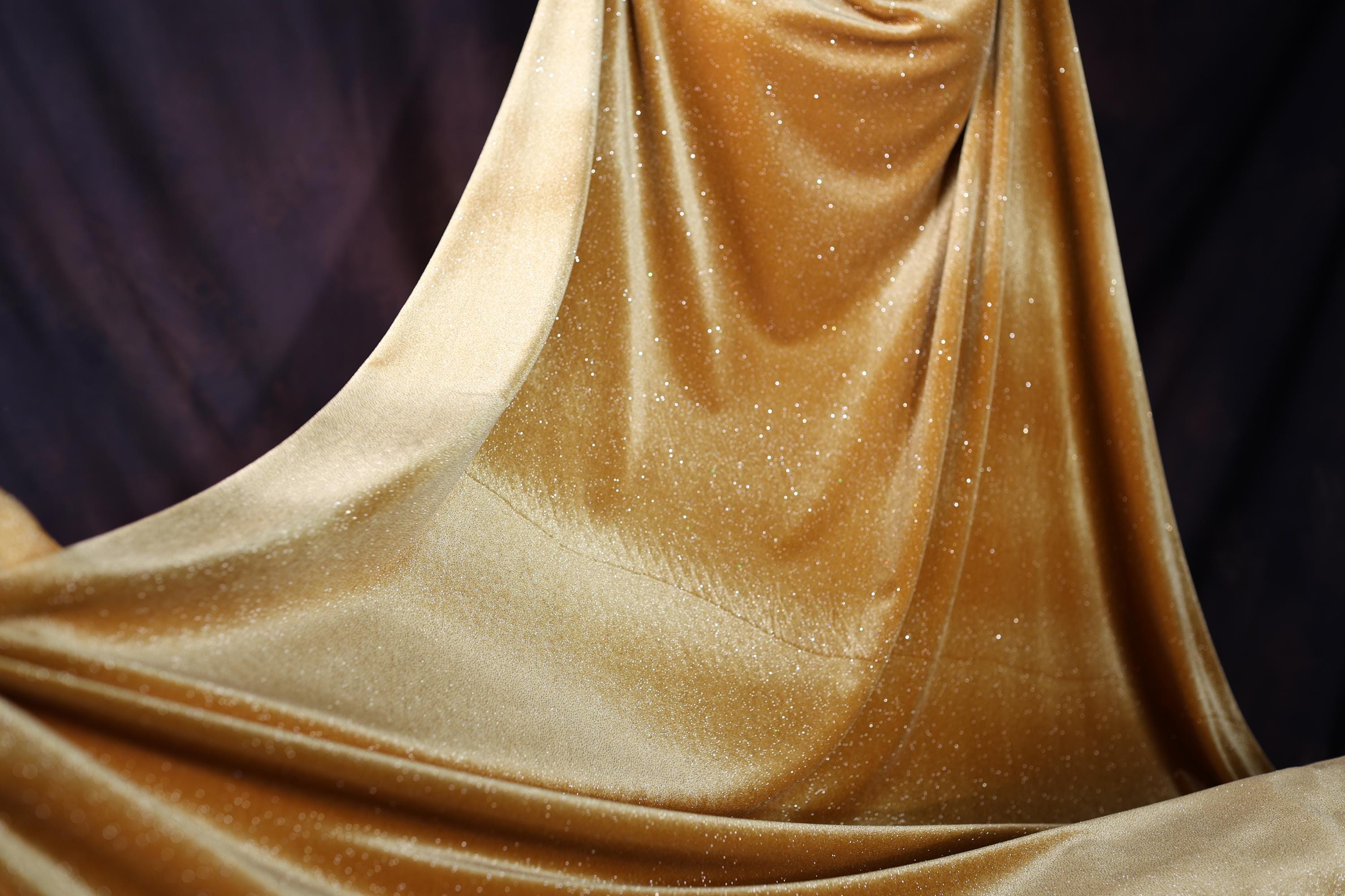 a woman in a gold dress standing in front of a black backdrop