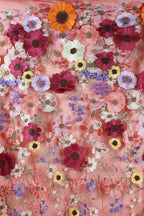 The image is a close-up of a fabric with a vibrant floral pattern, featuring a variety of colorful flowers such as red, orange, pink, purple, and yellow. The flowers are intricately embroidered or sewn onto the fabric, creating a visually striking and detailed design.