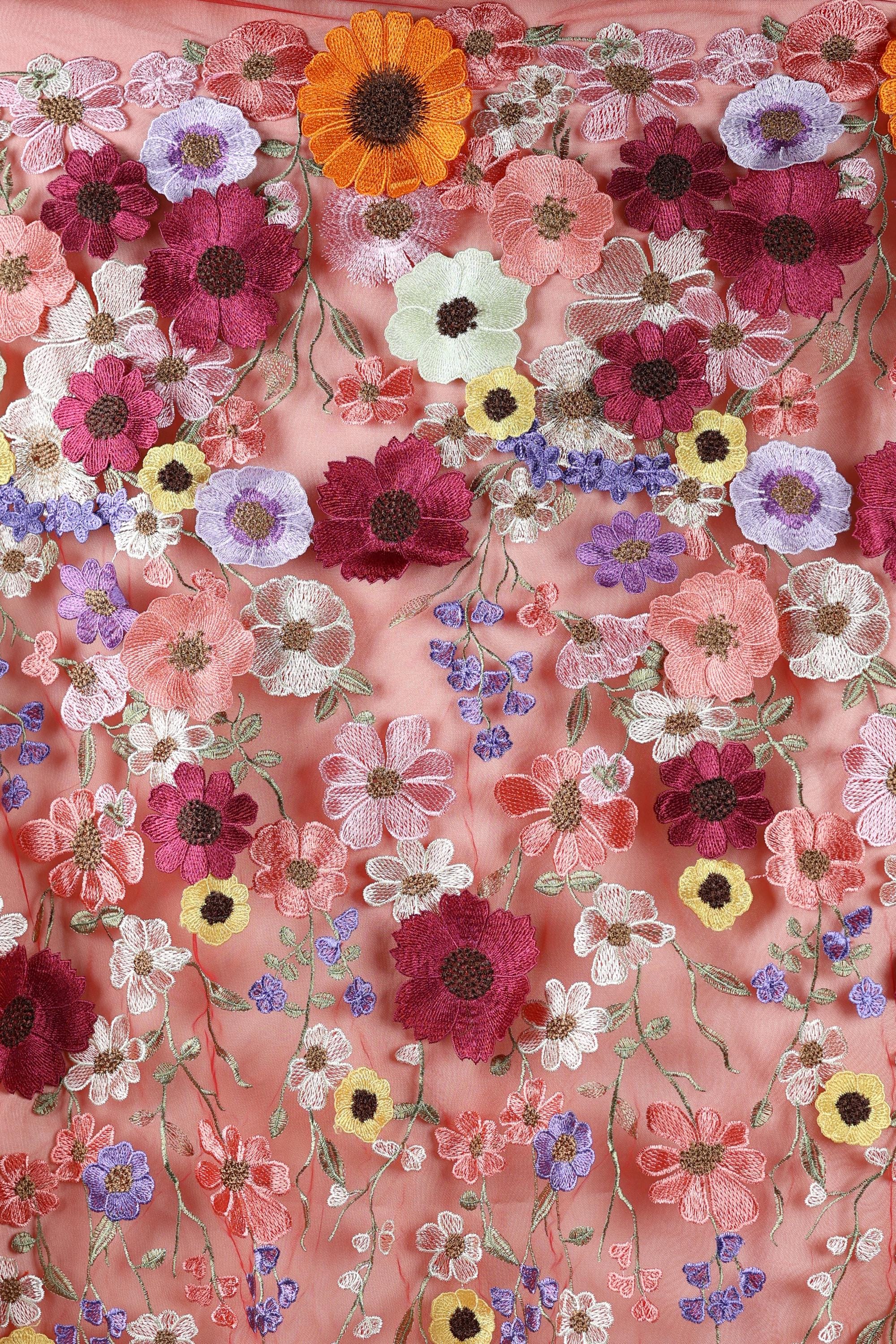 The image is a close-up of a fabric with a vibrant floral pattern, featuring a variety of colorful flowers such as red, orange, pink, purple, and yellow. The flowers are intricately embroidered or sewn onto the fabric, creating a visually striking and detailed design.