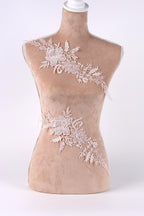 A mannequin with a beige body and white lace details on its torso, including floral and leaf-like patterns.