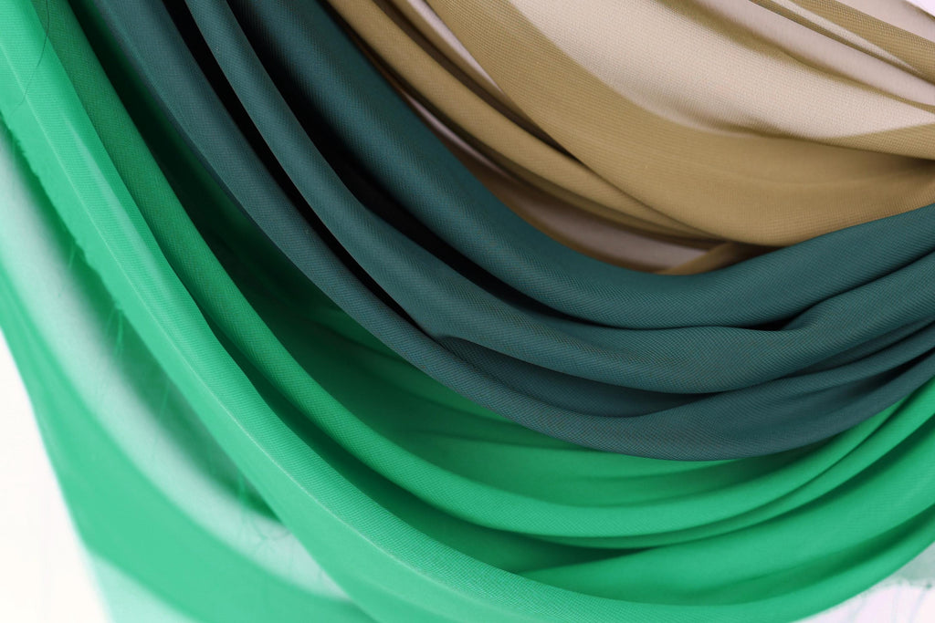 a close-up view of a pile of colorful fabric, with shades of green, blue, and brown. The fabric appears to be folded or draped in a way that creates a visually interesting and textured appearance.