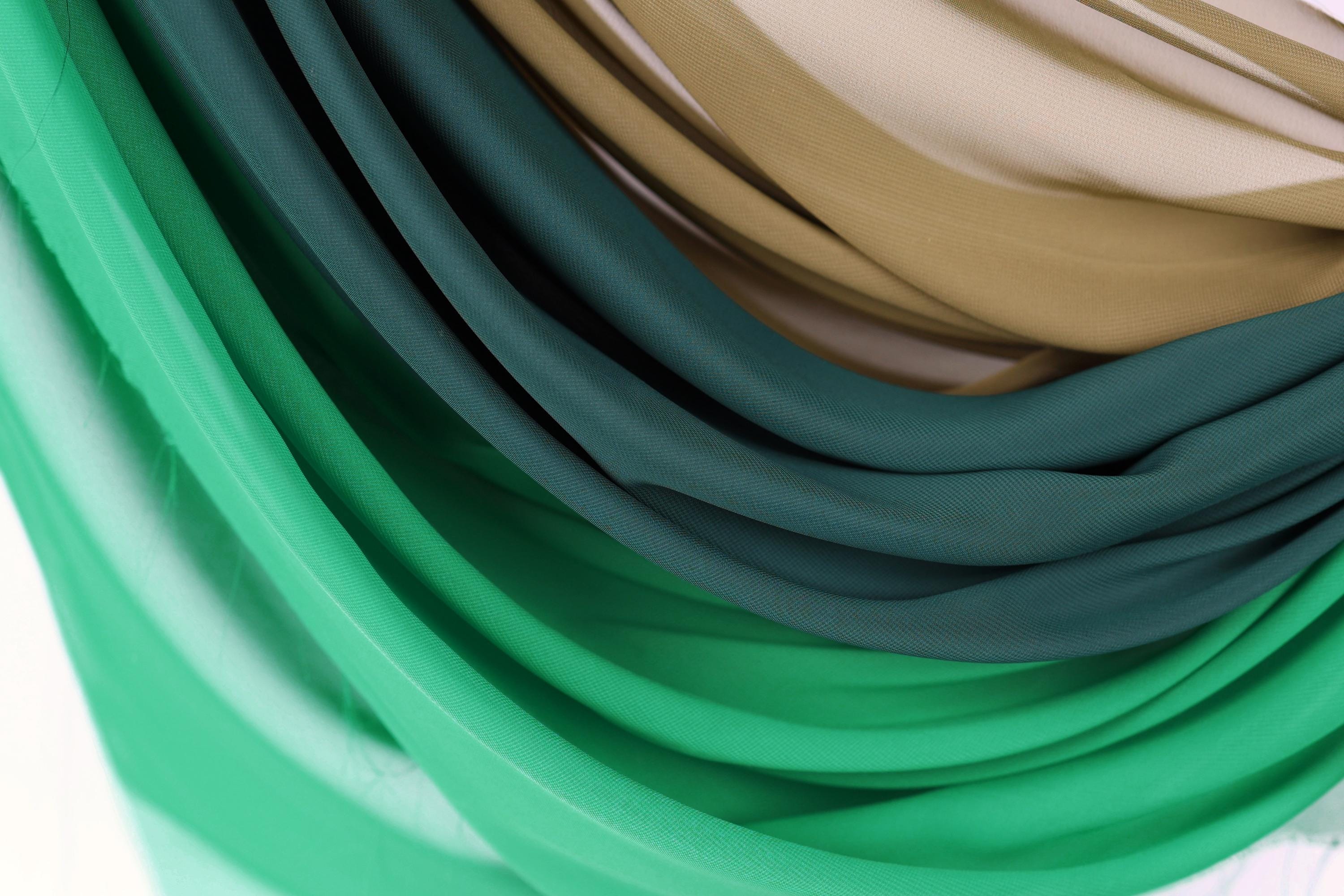 a close-up view of a pile of colorful fabric, with shades of green, blue, and brown. The fabric appears to be folded or draped in a way that creates a visually interesting and textured appearance.
