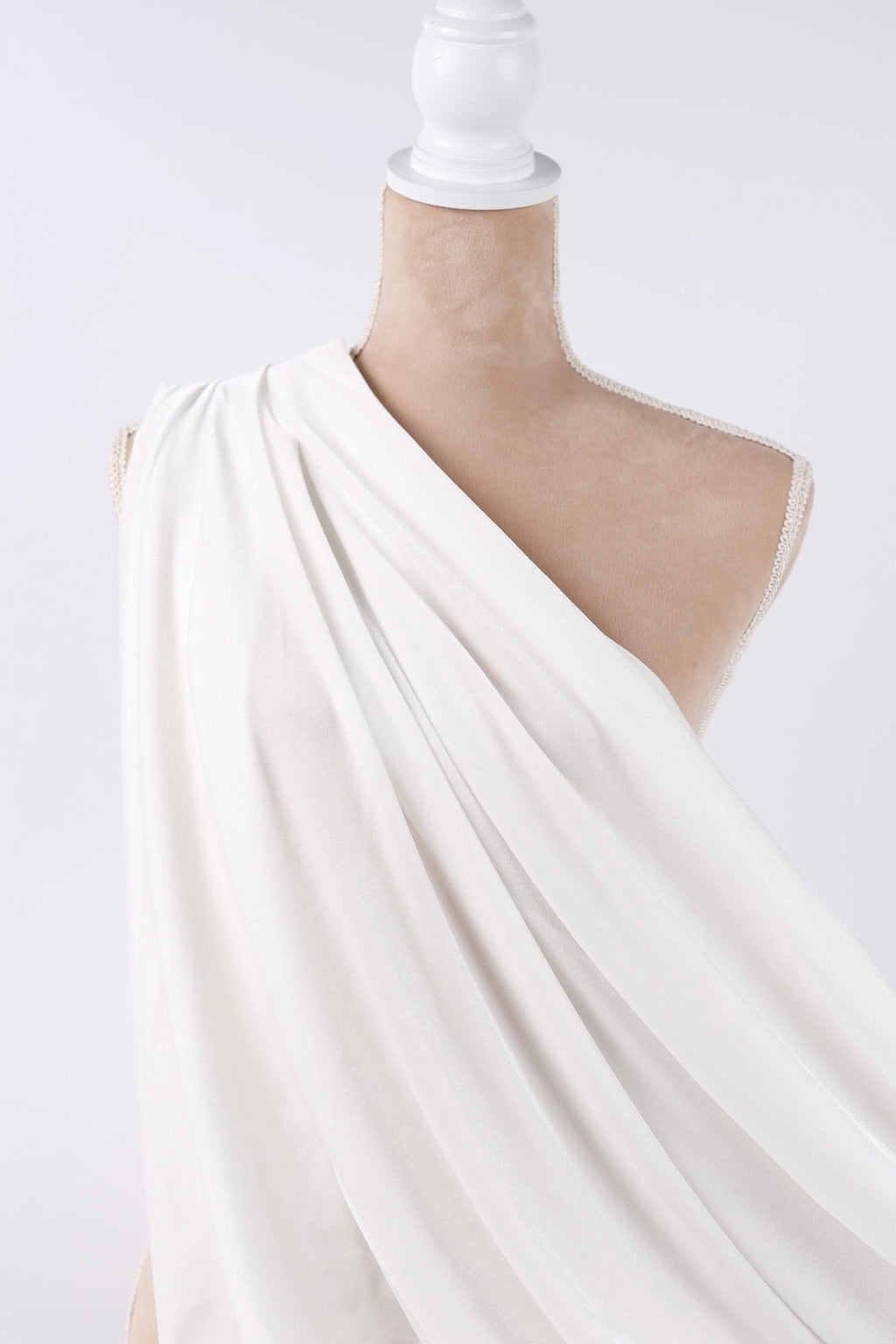 A mannequin wearing a white draped garment against a plain background.