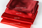 a stack of four red satin fabrics, each with a different color: Burgundy, Red, Red, and Tomato Lush.