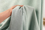 A hand is holding a light green fabric, possibly a piece of clothing or a textile, in front of a light green fabric.