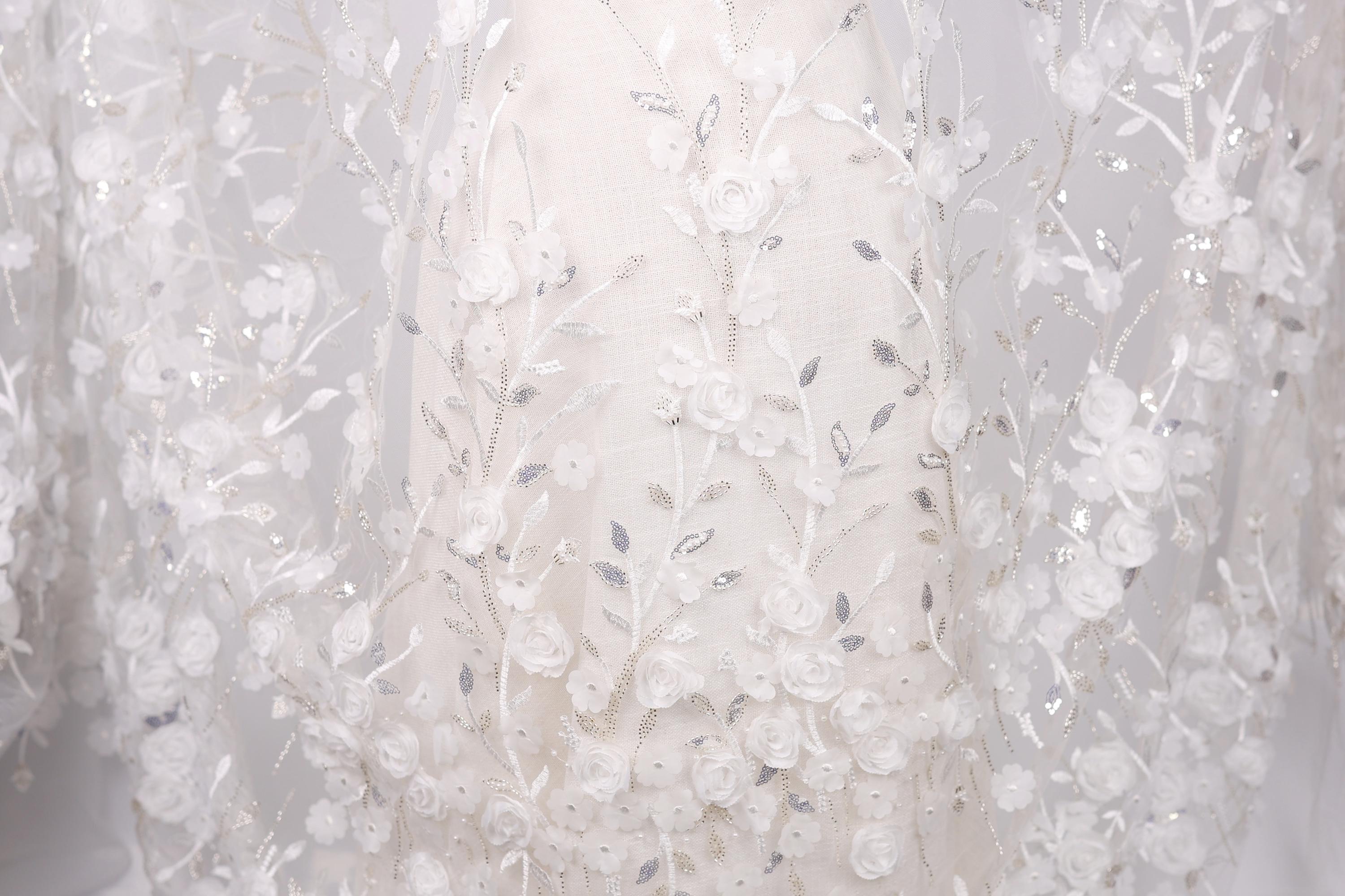 a close-up view of a delicate, white lace dress with intricate floral embroidery.