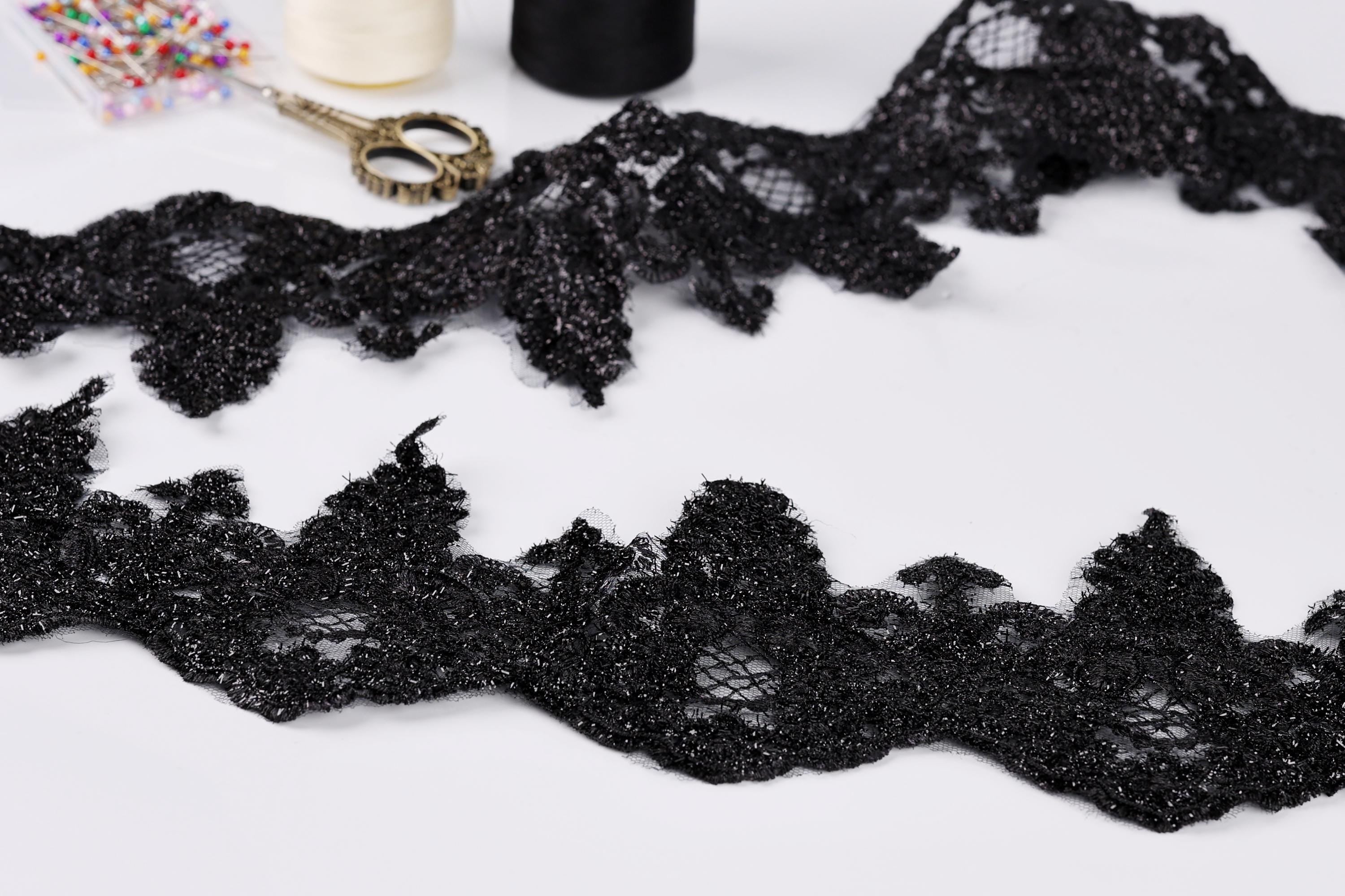 a close-up view of black lace fabric with a lace-like texture, along with sewing tools such as scissors and thread.