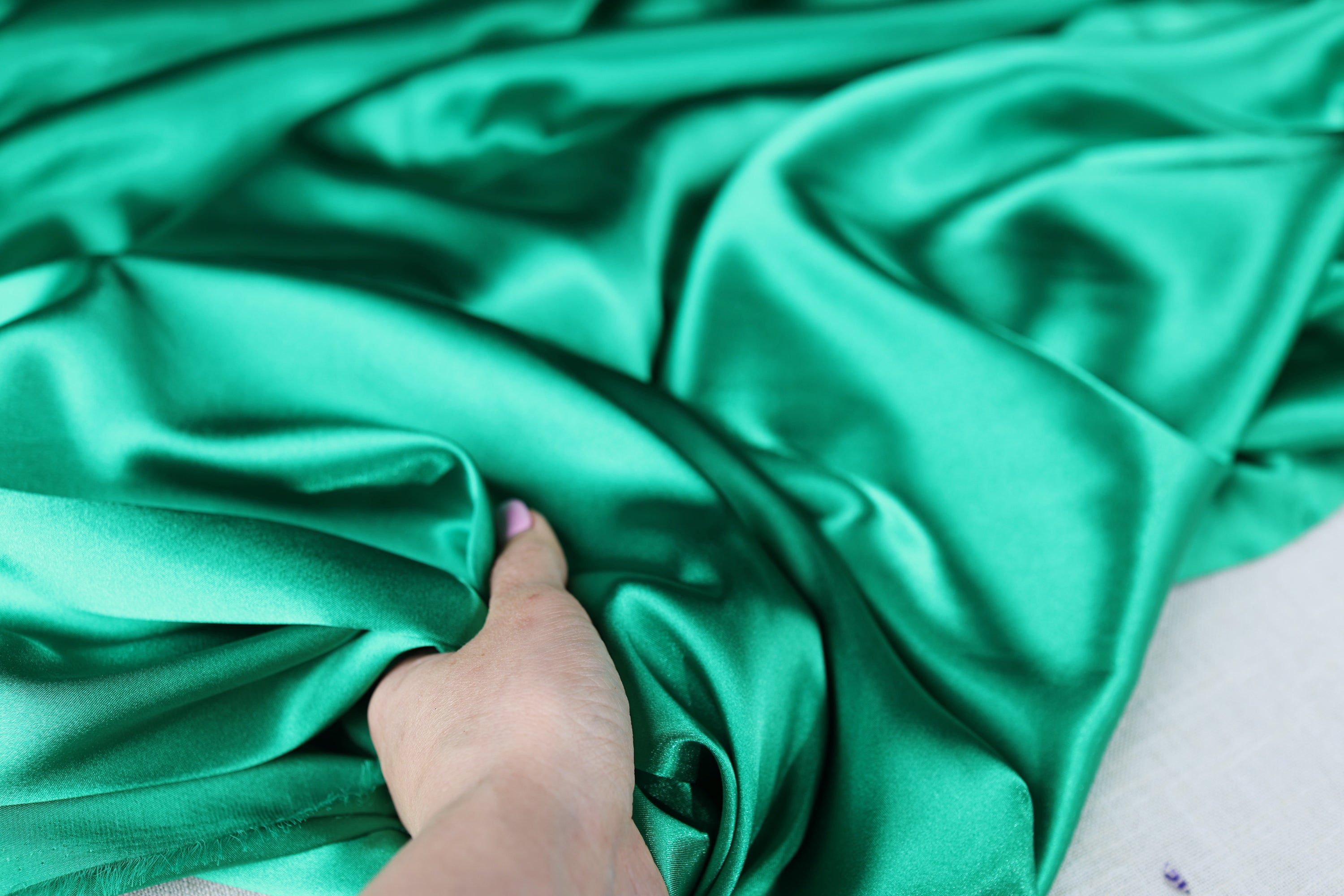 A hand is holding a piece of green satin fabric, which appears to be soft and smooth.