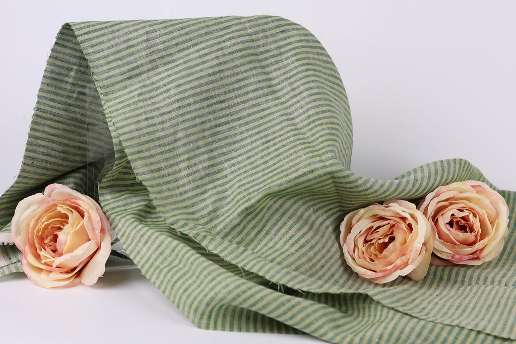a green and white striped fabric with three delicate pink roses resting on it.