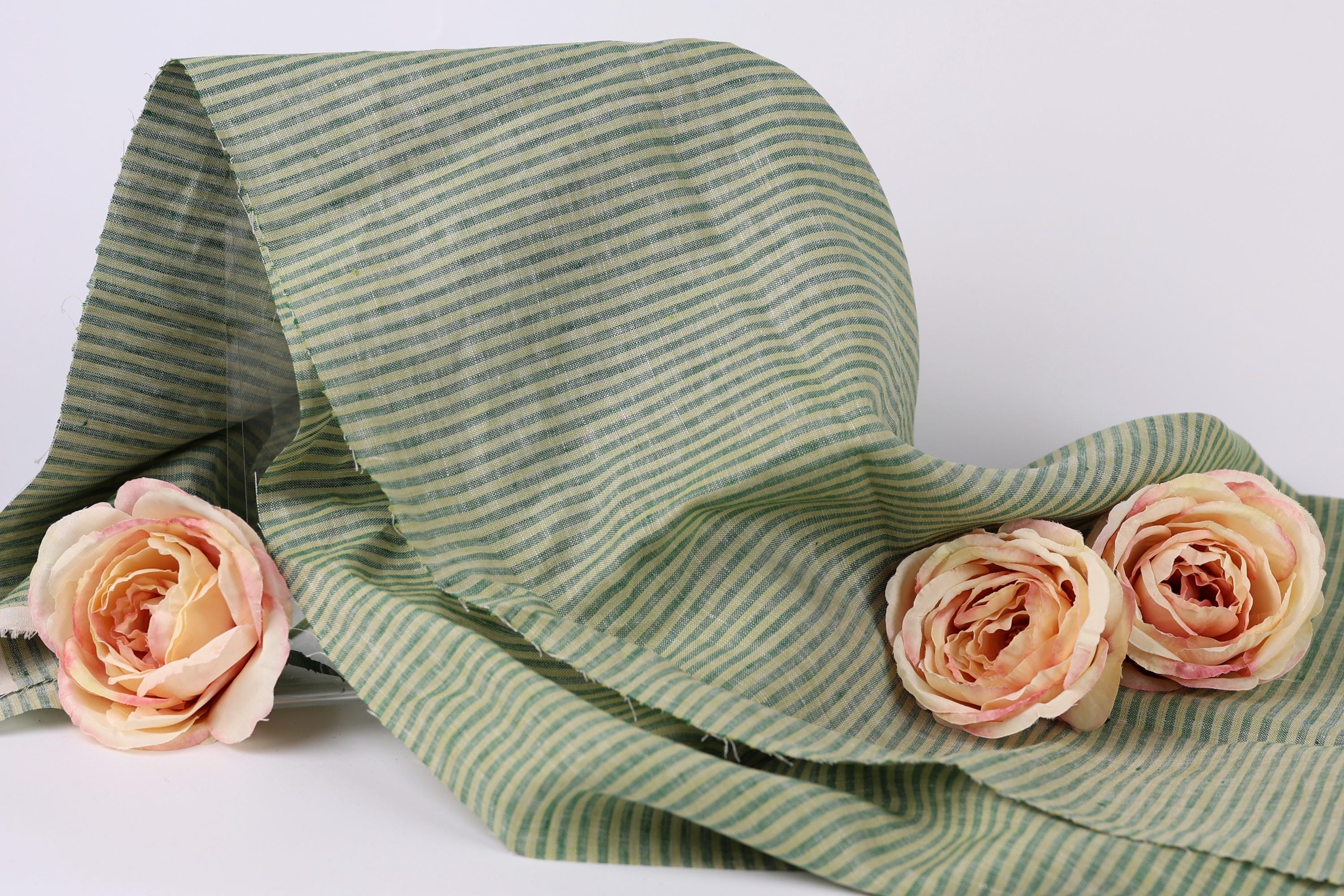a green and white striped fabric with three delicate pink roses resting on it.
