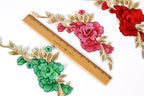 three floral embroidery pieces with different colors and designs, including red, pink, and green flowers, as well as leaves. A wooden ruler is placed between the floral pieces, indicating the size or dimensions of the embroidery.